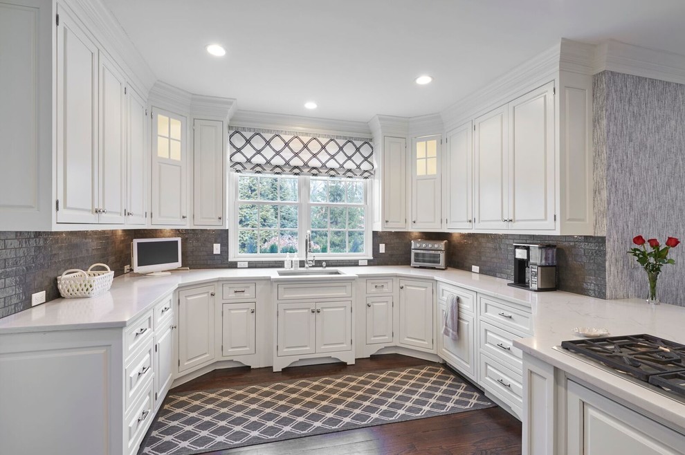 Example of a mid-sized classic u-shaped medium tone wood floor and brown floor eat-in kitchen design in New York with an undermount sink, raised-panel cabinets, white cabinets, quartz countertops, gray backsplash, glass tile backsplash, paneled appliances and a peninsula