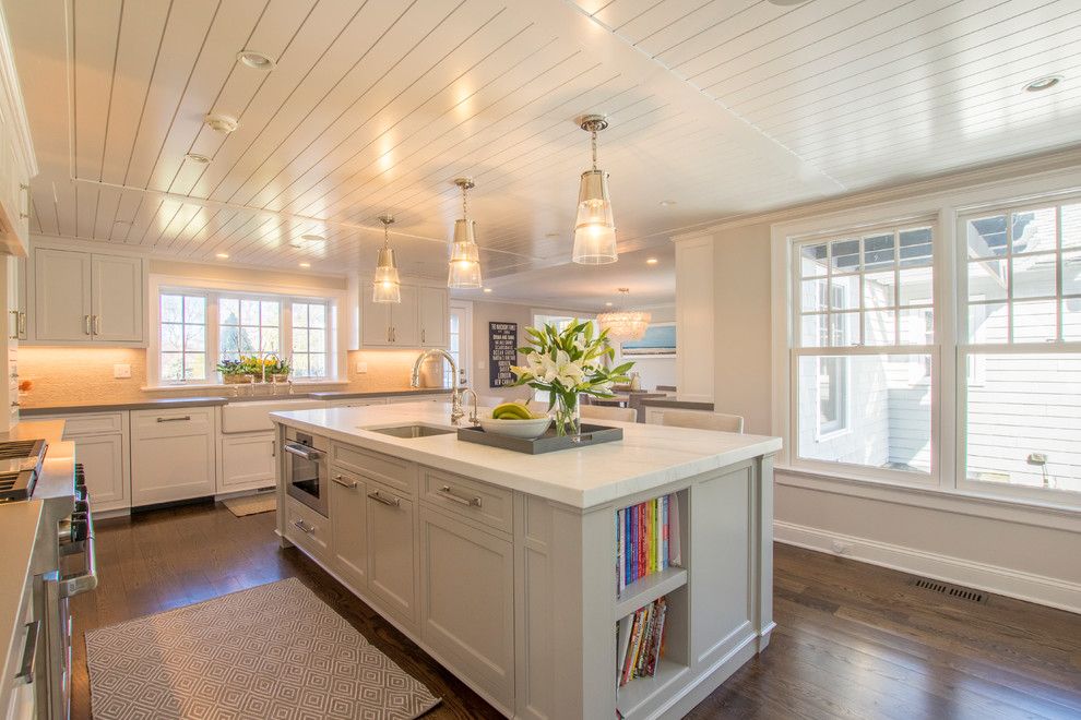 Transitional l-shaped medium tone wood floor and brown floor kitchen photo in New York with a farmhouse sink, shaker cabinets, white cabinets, stainless steel appliances, an island and white countertops