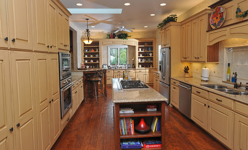 Inspiration for a large transitional galley medium tone wood floor eat-in kitchen remodel in Other with an island, raised-panel cabinets, yellow cabinets, quartz countertops, white backsplash, ceramic backsplash, stainless steel appliances and a triple-bowl sink