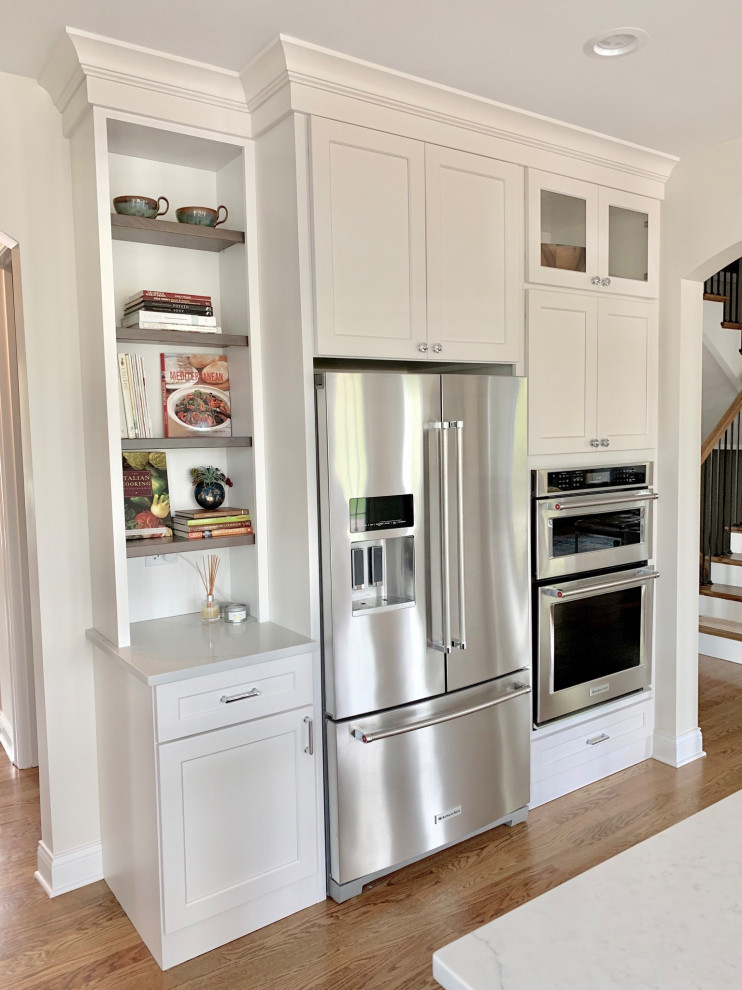 Inspiration for a mid-sized transitional l-shaped light wood floor and brown floor eat-in kitchen remodel in Chicago with an undermount sink, shaker cabinets, white cabinets, quartz countertops, white backsplash, porcelain backsplash, stainless steel appliances, an island and white countertops