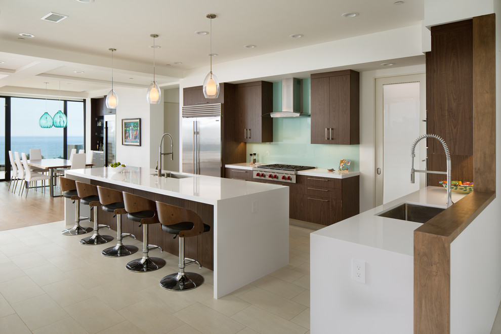 Offene Moderne Küche in U-Form mit Unterbauwaschbecken, flächenbündigen Schrankfronten, dunklen Holzschränken, Küchenrückwand in Blau, Glasrückwand, Küchengeräten aus Edelstahl, Kücheninsel und beigem Boden in San Diego