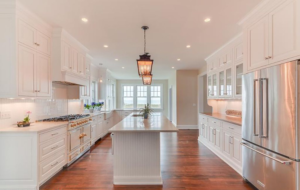 Inspiration for a large traditional galley kitchen in Philadelphia with a belfast sink, shaker cabinets, medium hardwood flooring, an island, white cabinets, white splashback and stainless steel appliances.