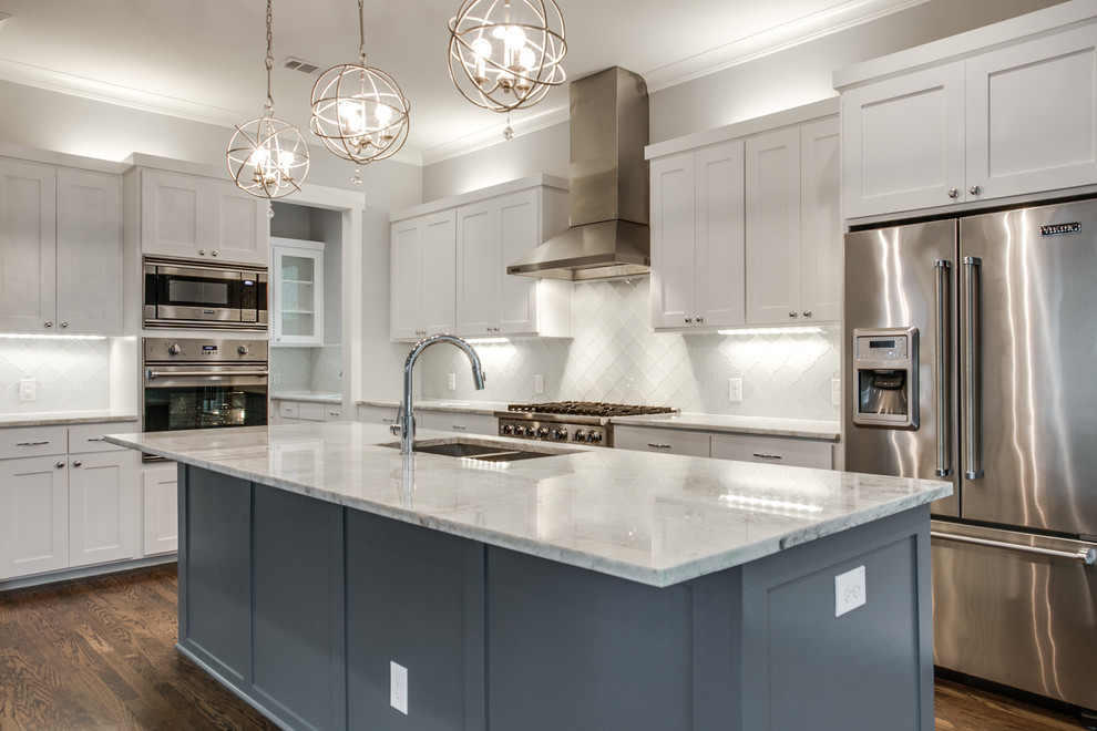 Inspiration for a large craftsman l-shaped medium tone wood floor kitchen remodel in Dallas with an undermount sink, shaker cabinets, white cabinets, quartzite countertops, white backsplash, glass tile backsplash, stainless steel appliances and an island