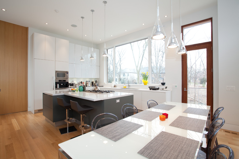 Mittelgroße Moderne Küche in L-Form mit flächenbündigen Schrankfronten, weißen Schränken, Küchenrückwand in Weiß, Elektrogeräten mit Frontblende, hellem Holzboden und Kücheninsel in Toronto