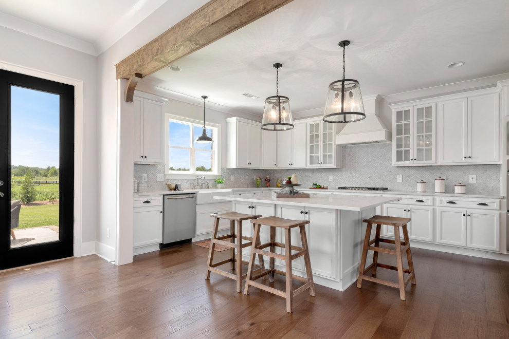 Traditional l-shaped open plan kitchen in Nashville with a belfast sink, shaker cabinets, white cabinets, grey splashback, stainless steel appliances, medium hardwood flooring, an island, brown floors and white worktops.