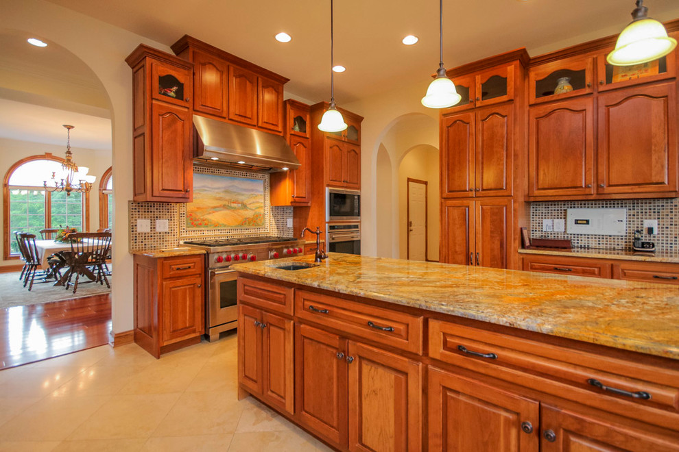 Example of a large classic u-shaped travertine floor and beige floor eat-in kitchen design in DC Metro with an undermount sink, raised-panel cabinets, medium tone wood cabinets, granite countertops, multicolored backsplash, mosaic tile backsplash, stainless steel appliances, an island and multicolored countertops