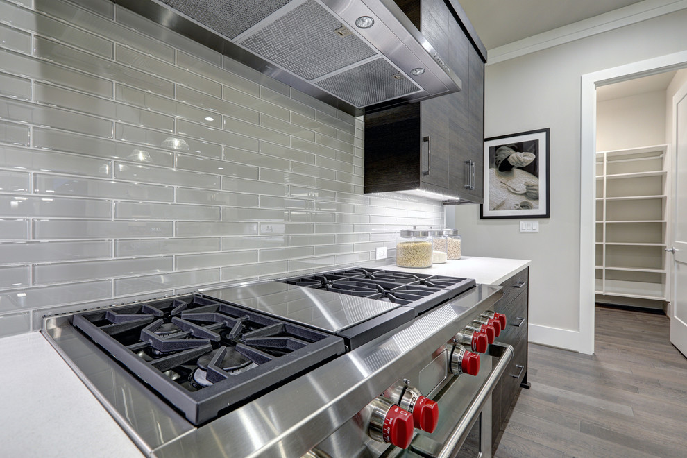 Enclosed kitchen - large modern u-shaped medium tone wood floor and gray floor enclosed kitchen idea in Chicago with flat-panel cabinets, dark wood cabinets, gray backsplash, glass tile backsplash, stainless steel appliances, an island and an undermount sink