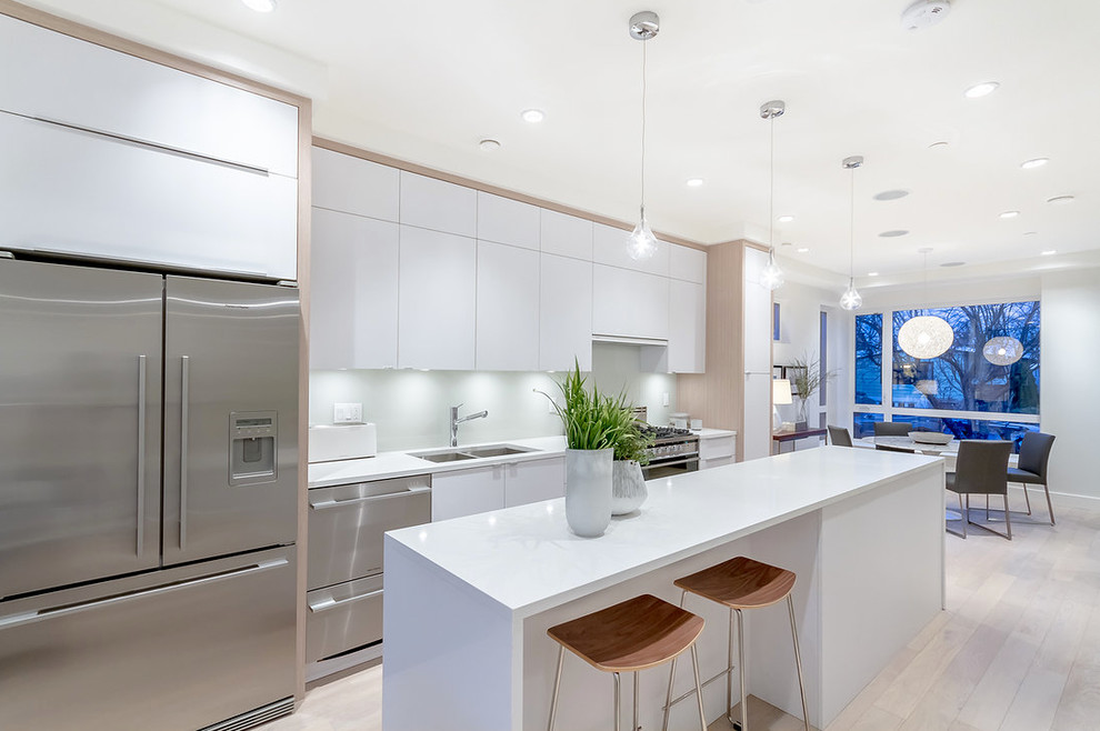 Eat-in kitchen - contemporary single-wall light wood floor eat-in kitchen idea in Vancouver with a double-bowl sink, flat-panel cabinets, white cabinets, white backsplash, stainless steel appliances and an island