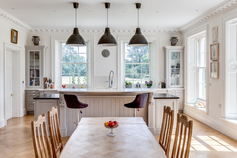 Inspiration for a traditional kitchen/diner in Gloucestershire with glass-front cabinets, grey cabinets, light hardwood flooring, an island, beige floors and white worktops.