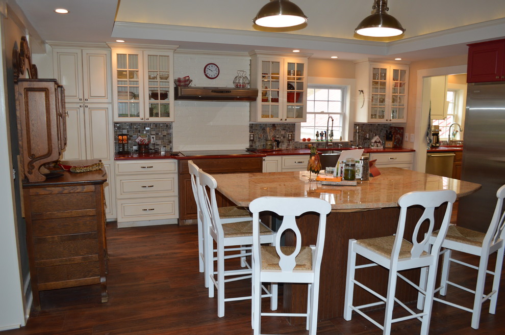 Example of a mid-sized country galley medium tone wood floor enclosed kitchen design in Philadelphia with a farmhouse sink, raised-panel cabinets, beige cabinets, quartzite countertops, beige backsplash, mosaic tile backsplash, stainless steel appliances and an island