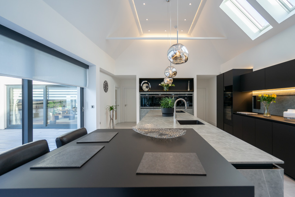 Design ideas for an expansive contemporary l-shaped kitchen with a submerged sink, flat-panel cabinets, black cabinets, grey splashback, integrated appliances, multiple islands, grey floors and grey worktops.
