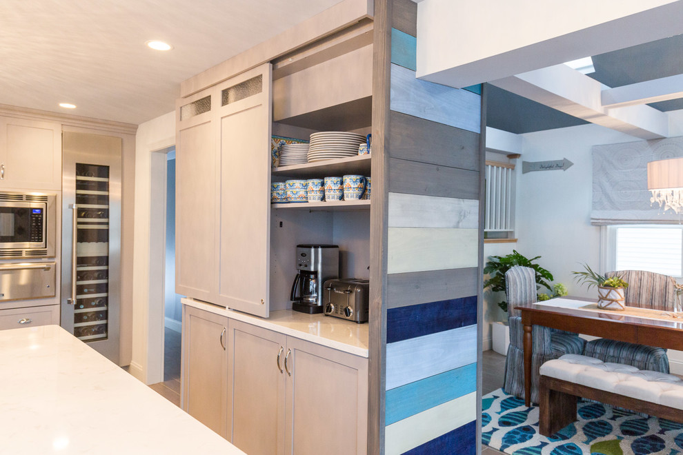 Bild på ett stort maritimt kök, med en undermonterad diskho, skåp i shakerstil, grå skåp, bänkskiva i kvarts, blått stänkskydd, glaspanel som stänkskydd, rostfria vitvaror, klinkergolv i porslin och en köksö