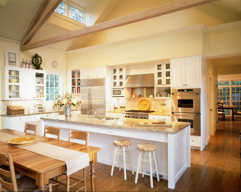 Foto på ett mycket stort lantligt kök, med luckor med glaspanel, vita skåp, granitbänkskiva, rostfria vitvaror, mellanmörkt trägolv, en köksö, en dubbel diskho och vitt stänkskydd