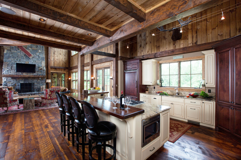 Inspiration for a large rustic single-wall dark wood floor open concept kitchen remodel in Burlington with an undermount sink, recessed-panel cabinets, white cabinets, granite countertops, beige backsplash, stone slab backsplash, paneled appliances and an island