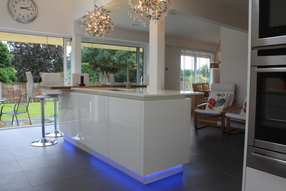 Eat-in kitchen - mid-sized modern porcelain tile eat-in kitchen idea in Hertfordshire with an undermount sink, flat-panel cabinets, white cabinets, quartz countertops, stainless steel appliances and an island
