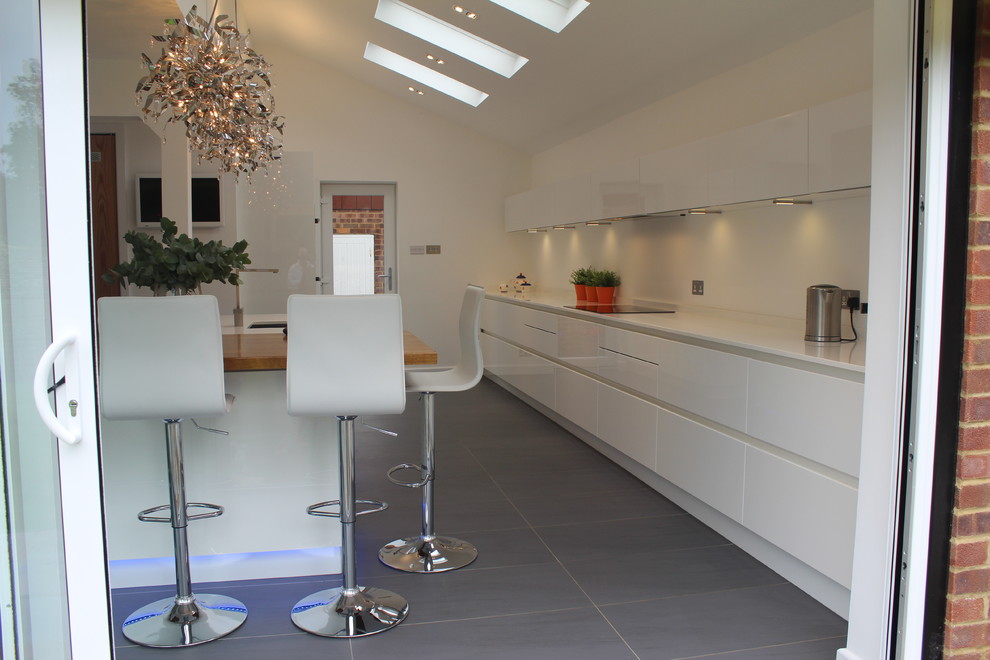 Example of a mid-sized minimalist porcelain tile eat-in kitchen design in Hertfordshire with an undermount sink, flat-panel cabinets, white cabinets, quartz countertops, stainless steel appliances and an island