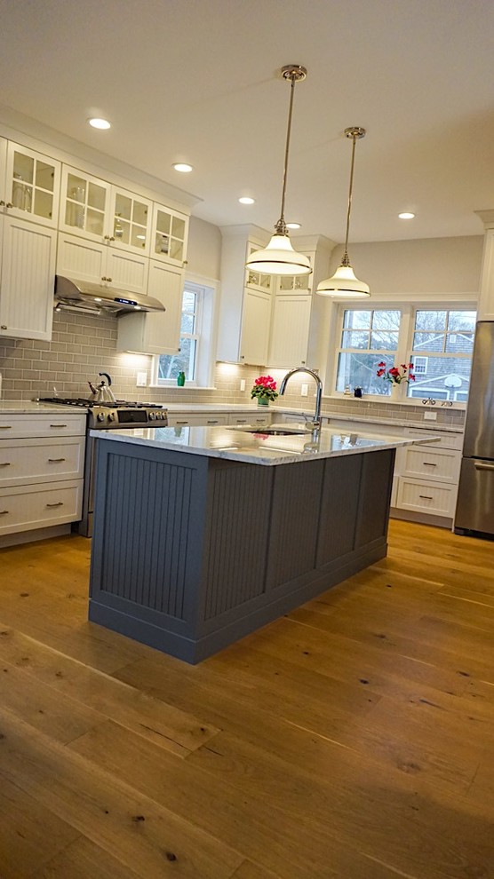 Example of a mid-sized transitional l-shaped dark wood floor and brown floor open concept kitchen design in Boston with an undermount sink, shaker cabinets, white cabinets, marble countertops, white backsplash, subway tile backsplash, stainless steel appliances and an island