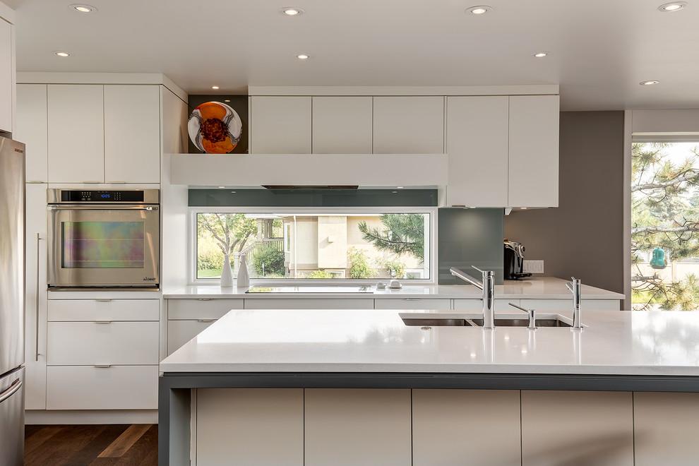 Moderne Küche mit Doppelwaschbecken, flächenbündigen Schrankfronten, weißen Schränken, Küchenrückwand in Grau, Glasrückwand, Küchengeräten aus Edelstahl, dunklem Holzboden und Kücheninsel in Calgary
