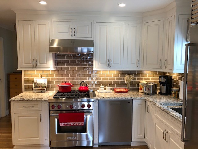 Inspiration for a mid-sized timeless l-shaped medium tone wood floor and brown floor enclosed kitchen remodel in New York with an undermount sink, raised-panel cabinets, white cabinets, granite countertops, brown backsplash, subway tile backsplash, stainless steel appliances, no island and multicolored countertops