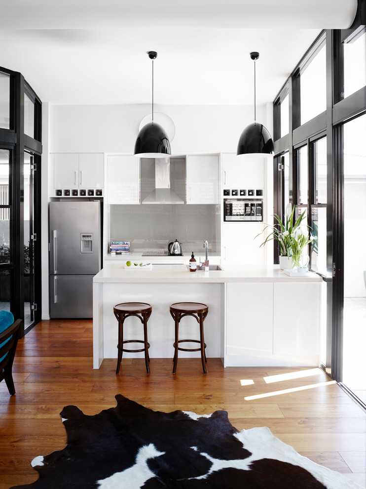 На фото: параллельная кухня в стиле неоклассика (современная классика) с врезной мойкой, плоскими фасадами, серым фартуком, фартуком из стекла, техникой из нержавеющей стали и черно-белыми фасадами