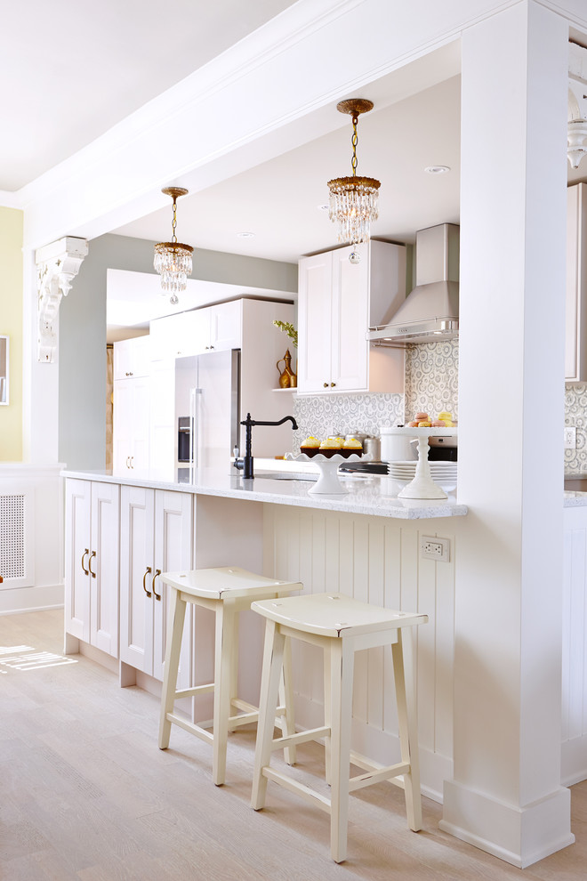 Diseño de cocina clásica con armarios con paneles empotrados, puertas de armario blancas, suelo de madera clara y una isla