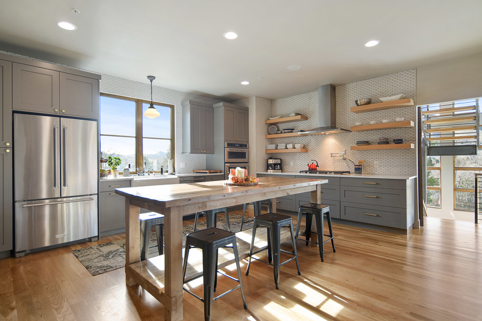Example of a mid-sized transitional l-shaped light wood floor and beige floor eat-in kitchen design in Denver with a farmhouse sink, shaker cabinets, gray cabinets, quartzite countertops, white backsplash, ceramic backsplash, stainless steel appliances and an island