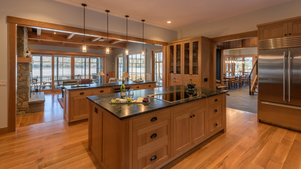 Example of a mountain style medium tone wood floor and brown floor kitchen design in Boston with an undermount sink, shaker cabinets, medium tone wood cabinets, stainless steel appliances, two islands and black countertops