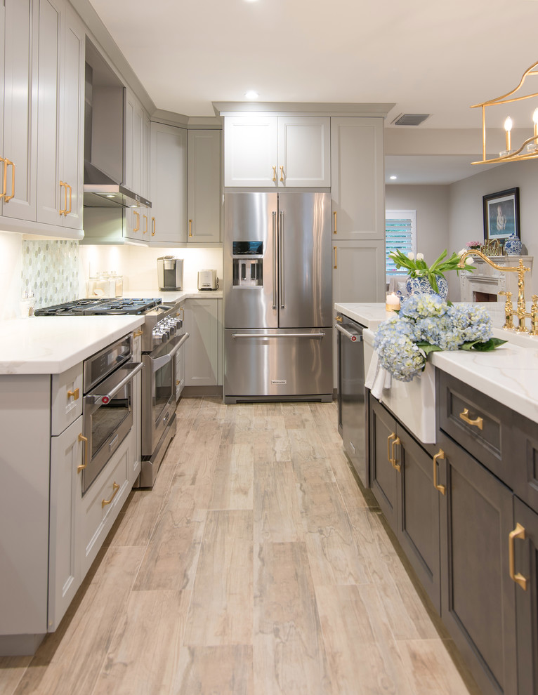 Bild på ett mellanstort lantligt vit vitt kök, med en rustik diskho, luckor med infälld panel, grå skåp, bänkskiva i kvarts, flerfärgad stänkskydd, stänkskydd i porslinskakel, rostfria vitvaror, laminatgolv, en köksö och brunt golv