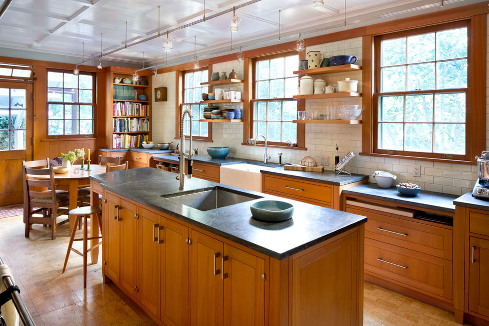 Classic galley kitchen/diner in New York with a belfast sink, medium wood cabinets, white splashback, metro tiled splashback, an island, beige floors and grey worktops.