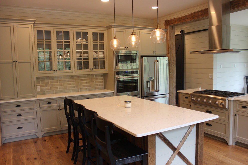 Bild på ett stort lantligt kök, med skåp i shakerstil, grå skåp, bänkskiva i kvarts, grått stänkskydd, stänkskydd i tunnelbanekakel, rostfria vitvaror, mellanmörkt trägolv, en köksö och brunt golv