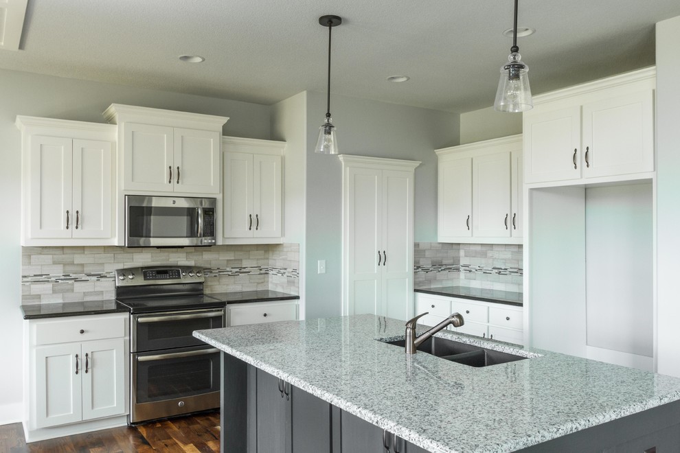 Example of a mid-sized minimalist medium tone wood floor kitchen design in Kansas City with an undermount sink, glass-front cabinets, white cabinets, granite countertops, multicolored backsplash, mosaic tile backsplash, stainless steel appliances and an island