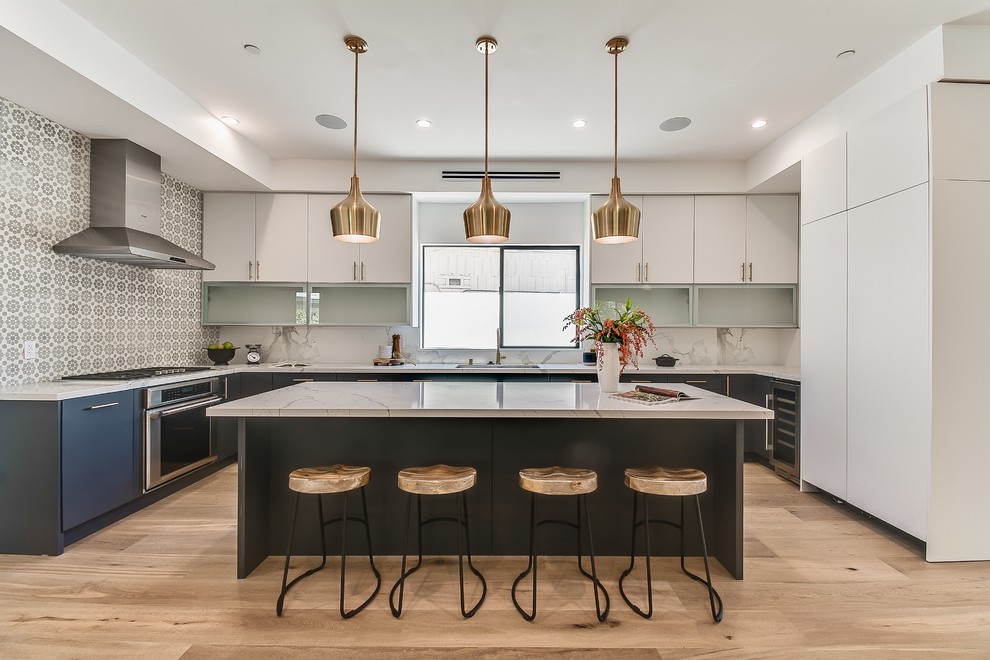 Example of a large beach style u-shaped light wood floor and beige floor open concept kitchen design in Los Angeles with flat-panel cabinets, blue cabinets, granite countertops, stainless steel appliances, an island, multicolored countertops, an undermount sink, gray backsplash and cement tile backsplash