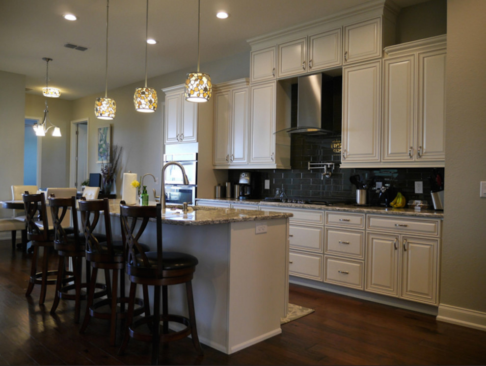 Mid-sized transitional galley dark wood floor and brown floor eat-in kitchen photo in Tampa with an undermount sink, raised-panel cabinets, white cabinets, granite countertops, black backsplash, subway tile backsplash, stainless steel appliances, an island and multicolored countertops
