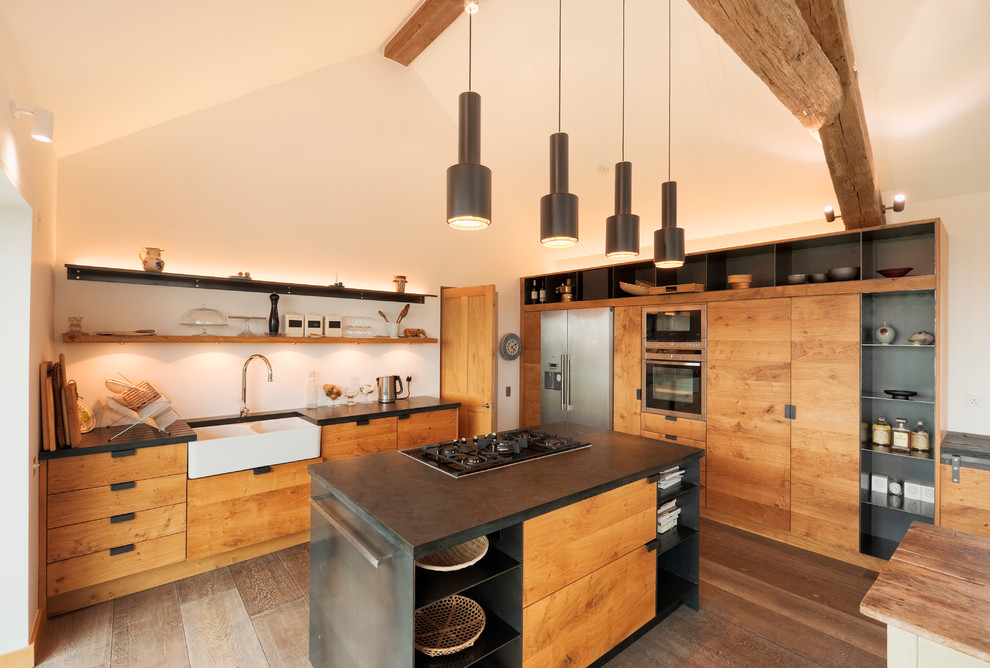 Exemple d'une grande cuisine tendance en L et bois brun avec un évier de ferme, un placard à porte plane, un électroménager en acier inoxydable, un sol en bois brun et îlot.