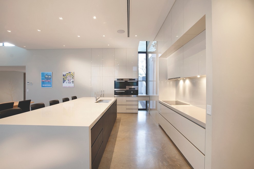 Exempel på ett modernt kök, med en undermonterad diskho, släta luckor, vita skåp, vitt stänkskydd, rostfria vitvaror och en köksö