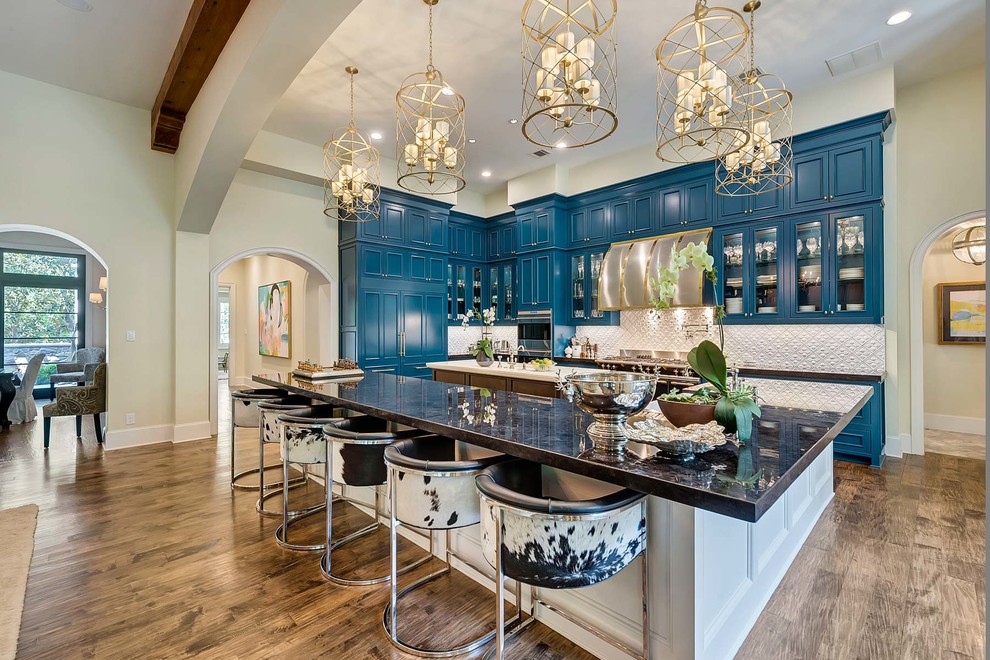 This is an example of a large contemporary l-shaped kitchen/diner in Dallas with a belfast sink, recessed-panel cabinets, blue cabinets, white splashback, stainless steel appliances, medium hardwood flooring, multiple islands, ceramic splashback and brown floors.