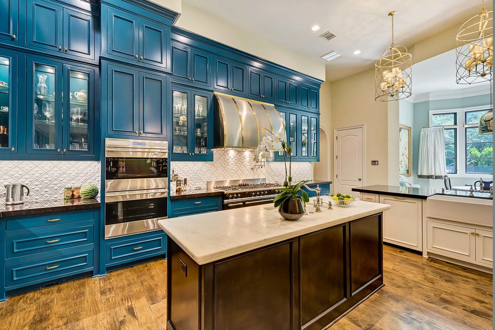 Large contemporary l-shaped kitchen/diner in Dallas with a belfast sink, recessed-panel cabinets, blue cabinets, white splashback, stainless steel appliances, medium hardwood flooring and multiple islands.