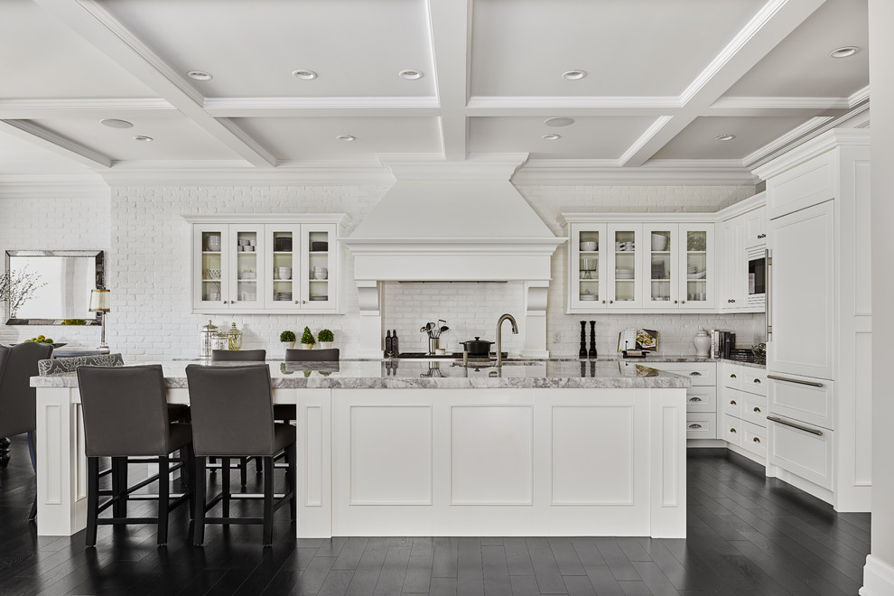 Large classic l-shaped open plan kitchen in Edmonton with shaker cabinets, white cabinets, engineered stone countertops, white splashback, metro tiled splashback, white appliances, an island, a submerged sink and painted wood flooring.