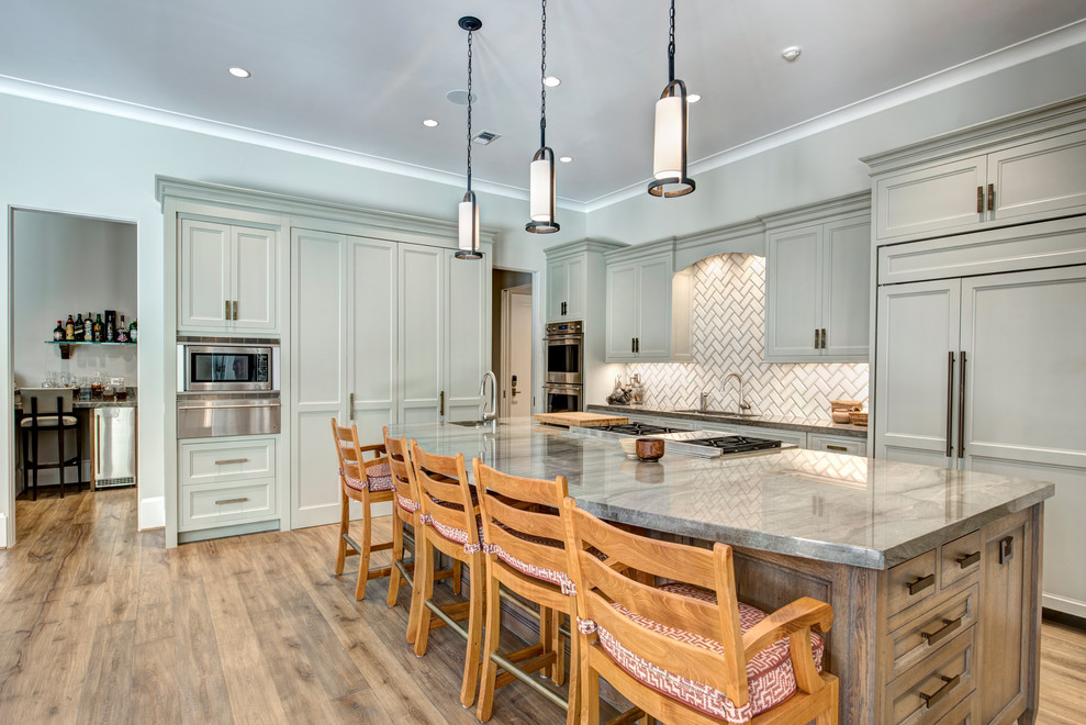 Foto på ett medelhavsstil grå l-kök, med en undermonterad diskho, luckor med infälld panel, grå skåp, vitt stänkskydd, integrerade vitvaror, mellanmörkt trägolv, en köksö och brunt golv