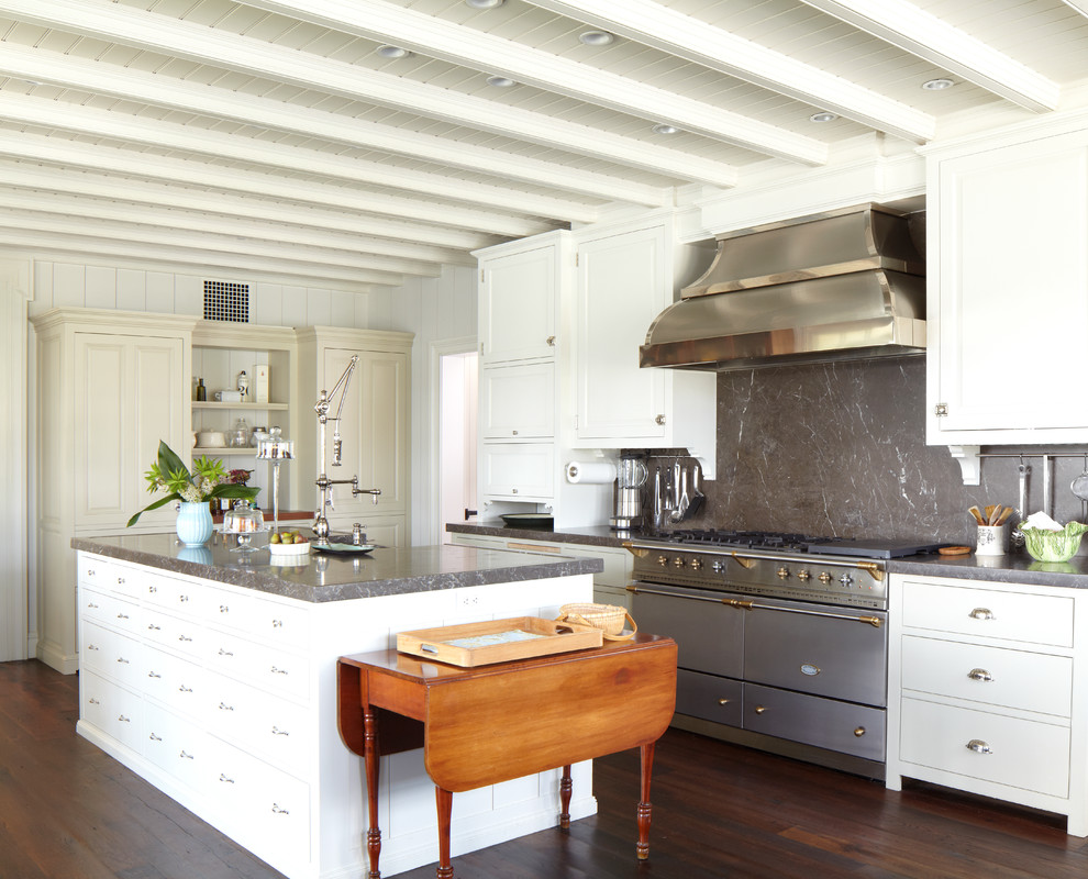 Example of a large classic single-wall dark wood floor and brown floor enclosed kitchen design in New York with marble countertops, a farmhouse sink, recessed-panel cabinets, white cabinets, gray backsplash, stone slab backsplash, stainless steel appliances and an island
