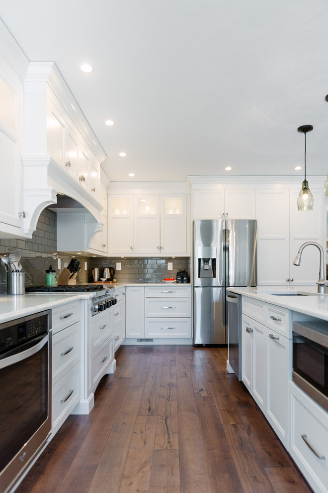 Example of a large transitional l-shaped medium tone wood floor and brown floor open concept kitchen design in Detroit with a single-bowl sink, flat-panel cabinets, white cabinets, quartz countertops, gray backsplash, glass tile backsplash, stainless steel appliances and an island