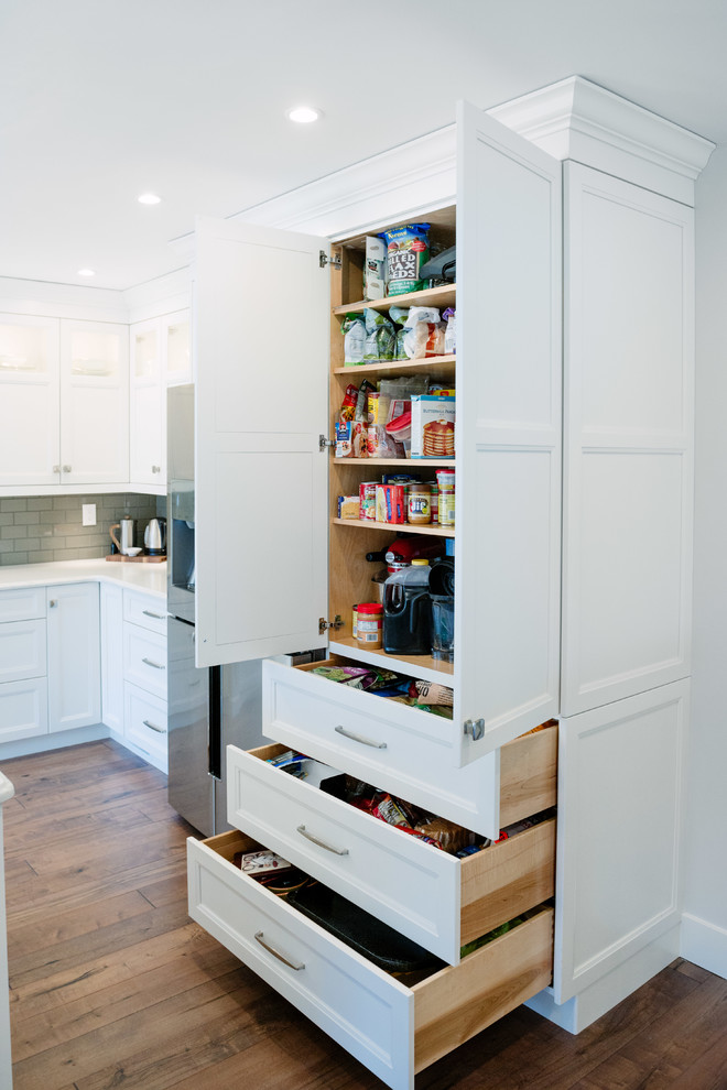 Open concept kitchen - large transitional l-shaped medium tone wood floor and brown floor open concept kitchen idea in Detroit with a single-bowl sink, flat-panel cabinets, white cabinets, quartz countertops, gray backsplash, glass tile backsplash, stainless steel appliances and an island