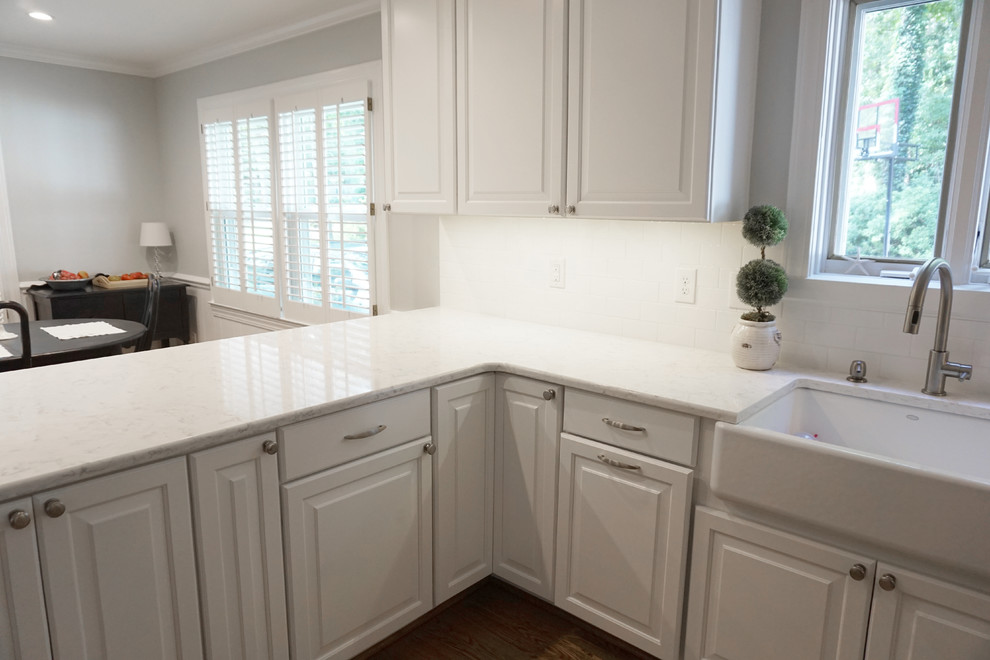 Example of a mid-sized country u-shaped medium tone wood floor eat-in kitchen design in Charlotte with a farmhouse sink, shaker cabinets, white cabinets, quartzite countertops, white backsplash, ceramic backsplash, stainless steel appliances and a peninsula