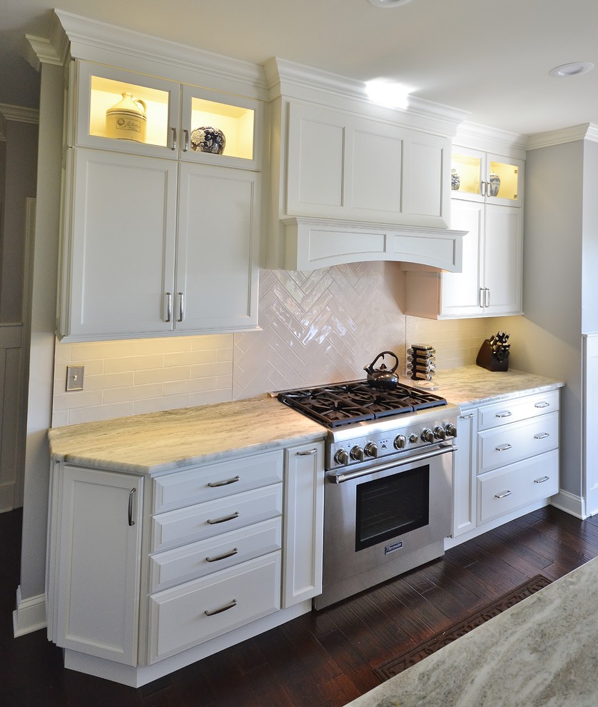 Photo of an expansive traditional l-shaped kitchen/diner in Philadelphia with a submerged sink, raised-panel cabinets, white cabinets, granite worktops, white splashback, metro tiled splashback, integrated appliances, dark hardwood flooring, an island and brown floors.