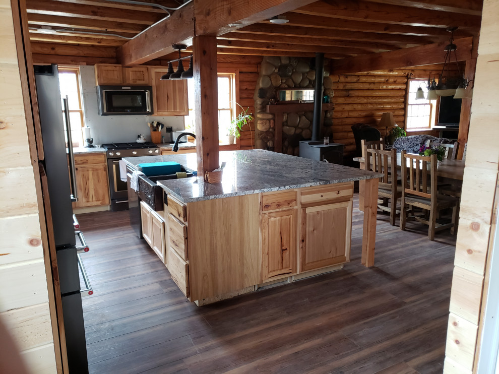 This is an example of a l-shaped kitchen/diner in Other with a belfast sink, raised-panel cabinets, light wood cabinets, granite worktops, stainless steel appliances, laminate floors, an island and brown floors.