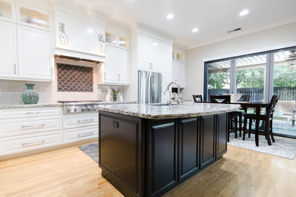 Bild på ett mellanstort lantligt linjärt kök och matrum, med en undermonterad diskho, luckor med upphöjd panel, vita skåp, granitbänkskiva, vitt stänkskydd, stänkskydd i keramik, rostfria vitvaror, ljust trägolv, en köksö och beiget golv