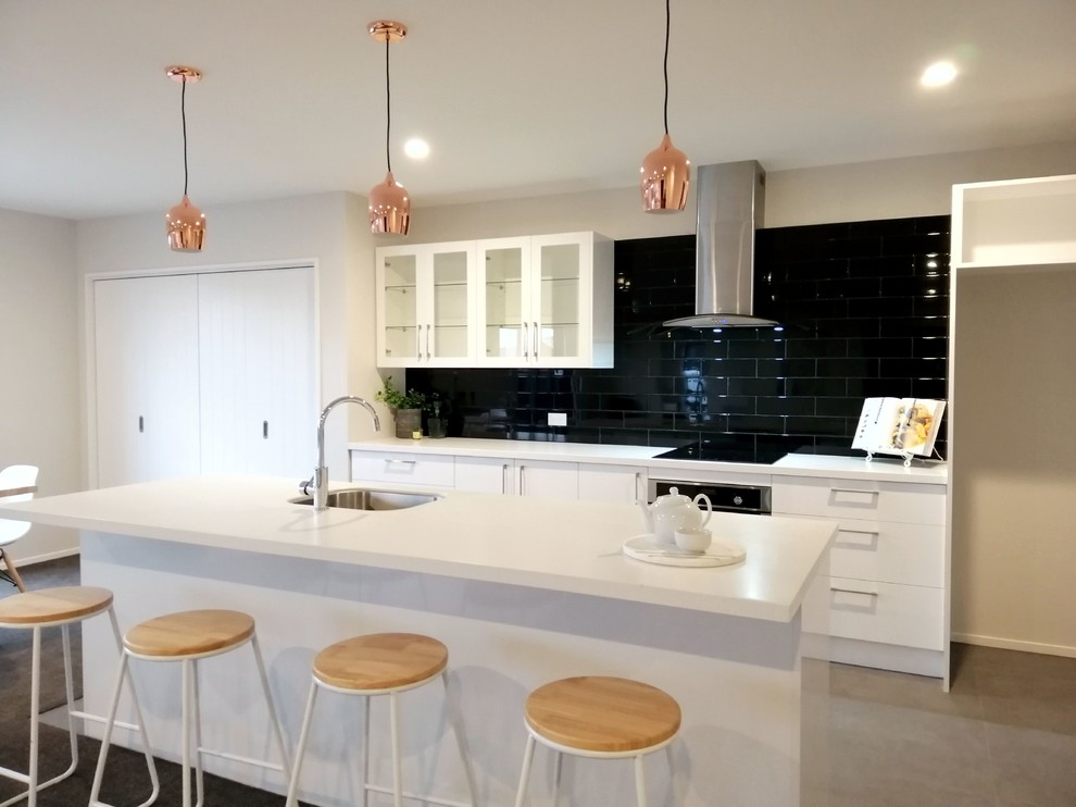 Design ideas for a large contemporary galley open plan kitchen in Christchurch with a belfast sink, glass-front cabinets, white cabinets, laminate countertops, black splashback, ceramic splashback, stainless steel appliances, lino flooring, an island, grey floors and white worktops.