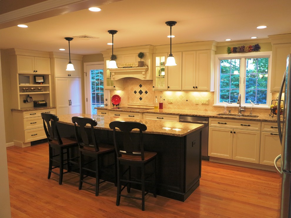 Example of a large classic l-shaped medium tone wood floor eat-in kitchen design in Bridgeport with a double-bowl sink, recessed-panel cabinets, beige cabinets, granite countertops, beige backsplash, stone tile backsplash, stainless steel appliances and an island