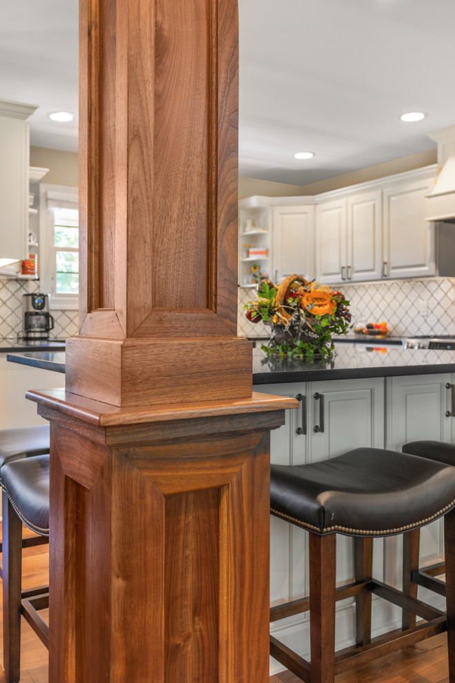Inspiration for a large traditional u-shaped kitchen/diner in Milwaukee with dark hardwood flooring, brown floors, a belfast sink, raised-panel cabinets, white cabinets, engineered stone countertops, white splashback, ceramic splashback, stainless steel appliances, an island and black worktops.