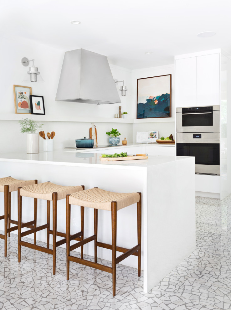 Cette image montre une cuisine design en U avec un placard à porte plane, des portes de placard blanches, un électroménager en acier inoxydable, une péninsule, un sol blanc et un plan de travail blanc.